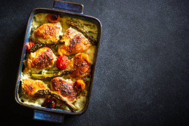 Kuşkonmaz ve kremalı soslu sebzeli fırında tavuk butları. Fotokopi alanı koyu arkaplanda düz yatıyordu.