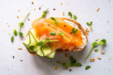 Krem peynirli, somonlu ve salatalıklı sandviç. Beyaz masadaki üst görünüm.