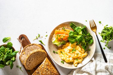 Çırpılmış yumurta, krem peynirli sandviç, somon balığı ve beyaz taş masada salata yaprakları. Kuzey diyeti. Kopyalama alanı olan üst görünüm.