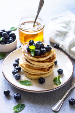 Beyaz taş masada taze yaban mersinli krep ve bal yığını..