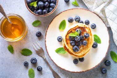 Taş masada taze yaban mersinli krep ve bal yığını. Sağlıklı kahvaltı ya da tatlı. Kopyalama alanı olan üst görünüm.