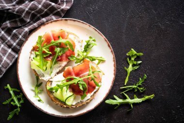 Krem peynirli ve jambonlu sandviç ya da taze yeşillikli beyaz tabak. Koyu masadaki üst görünüm.