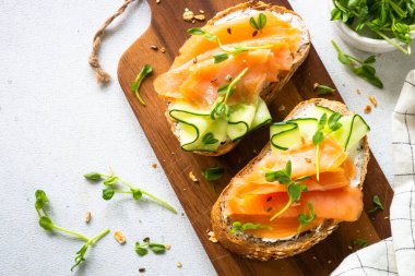 Krem peynirli, somonlu ve salatalıklı sandviç. Beyaz masadaki üst görünüm.