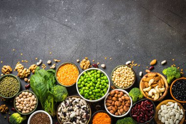 Vegan protein kaynağı. Baklagiller, fasulyeler, fındıklar, sebzeler ve tohumlar. Siyah taş masadaki en üst manzara. Sağlıklı vejetaryen yemekleri.