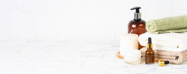 Beyaz banyodaki spa arka planı. Bir yığın havlu, şampuan şişesi, gerekli yağ ve kozmetik ürünleri. Uzun pankart biçimi.