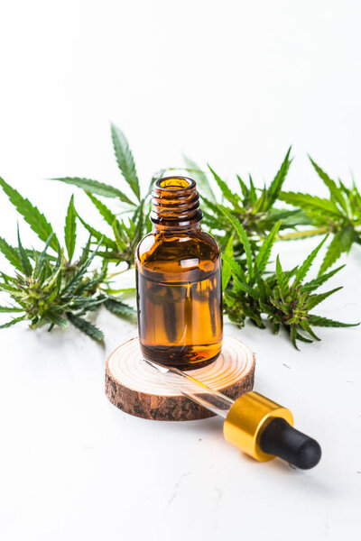 КБР масло в стеклянных бутылках и листья конопли за белым столом. Закрывай. Медицина и косметика.