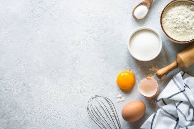 Arkaplan malzemeleri pişiriyorum. Un, şeker, yumurta ve diğer şeyler hafif taş masada. Kopyalama alanı olan üst görünüm.