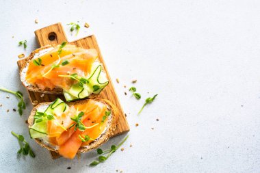 Krem peynirli, somonlu ve salatalıklı sandviç. Beyaz masadaki üst görünüm.