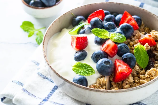 Greek Yogurt with granola and fresh berries at white table.