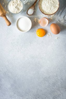 Arkaplan malzemeleri pişiriyorum. Un, şeker, yumurta ve diğer şeyler hafif taş masada. Kopyalama alanı olan üst görünüm.