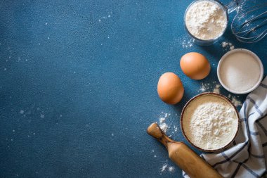 Mavi taş masada fırın arka planı. Un, şeker, yumurta ve çatal bıçak. Kopyalama alanı olan üst görünüm.