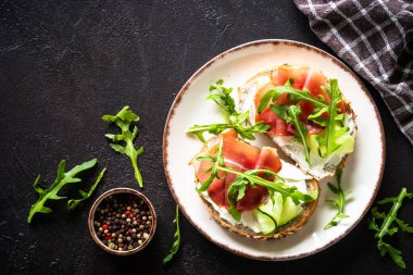 Krem peynirli ve jambonlu sandviç ya da taze yeşillikli beyaz tabak. Koyu tabloda kopyalama alanı olan üst görünüm.
