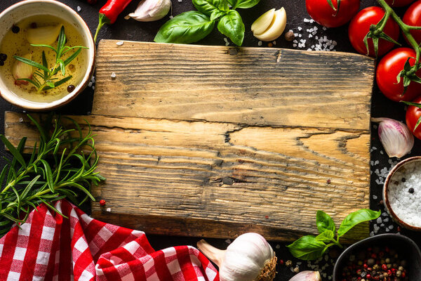Food background. Oak cutting board, vegetables, herbs, spices at dark kitchen table. Top view with space for design.