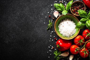 Sebzeler, otlar ve baharatlarla dolu siyah taş masada yemek. Kopyalama alanı olan üst görünüm.