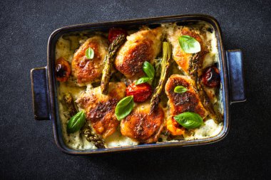 Pişmiş tavuk butları kuşkonmaz ve siyah masada krema soslu domatesler..