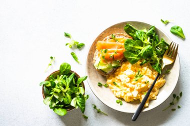Sağlıklı kahvaltı ya da öğle yemeği. Çırpılmış yumurta, krem peynirli sandviç, somon balığı ve beyaz taş masada salata yaprakları. Kopyalama alanı olan üst görünüm.