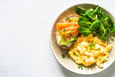 Çırpılmış yumurta, krem peynirli sandviç, somon balığı ve salata yaprakları. Kopyalama alanı olan üst görünüm.