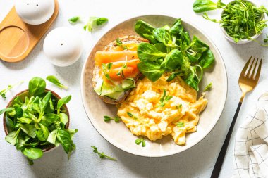 Sağlıklı kahvaltı ya da öğle yemeği. Çırpılmış yumurta, krem peynirli sandviç, somon balığı ve beyaz taş masada salata yaprakları. Kopyalama alanı olan üst görünüm.