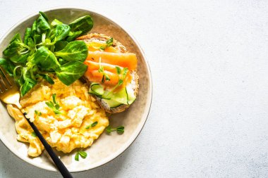 Çırpılmış yumurta, krem peynirli sandviç, somon balığı ve beyaz taş masada salata yaprakları. Üst görünüm.