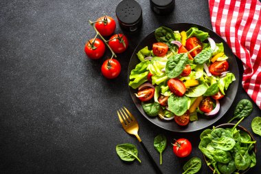 Taze sebzeli yeşil salata ve siyah arka planda yeşil yapraklar. Kopyalama alanı olan üst görünüm.