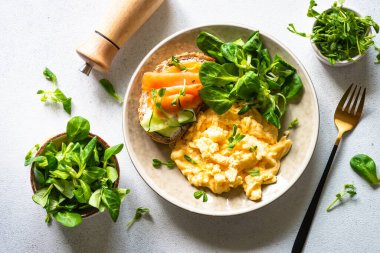 Çırpılmış yumurta, krem peynirli sandviç, somon balığı ve beyaz taş masada salata yaprakları. Üst görünüm.