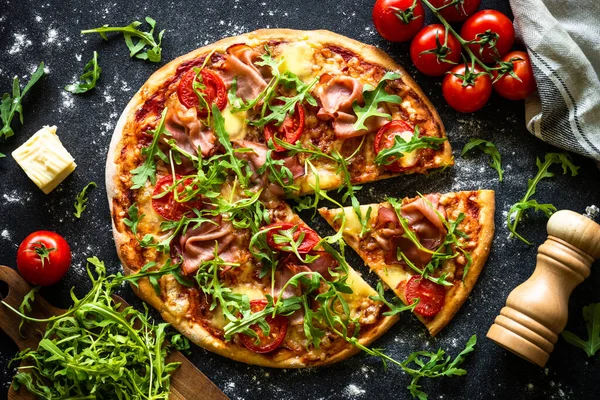 黒を背景にピザ プロシュート チーズ トマト アルグラを具材とした伝統的なイタリアのピザ トップ表示 — ストック写真