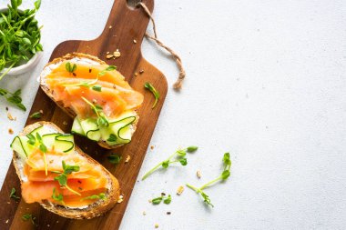 Krem peynirli, somonlu ve salatalıklı sandviç. Beyaz masadaki üst görünüm.