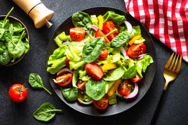 Taze sebzeli yeşil salata ve siyah arka planda yeşil yapraklar. Kopyalama alanı olan üst görünüm.