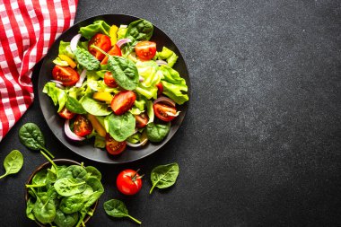 Taze sebzeli salata ve siyah arka planda yeşil salata yaprakları. Kopyalama alanı olan en üst görüntü.