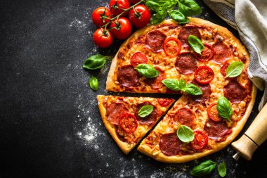 Siyah arka planda pizza. Salam peynirli, domatesli ve fesleğenli geleneksel İtalyan pizzası. Kopyalama alanı olan üst görünüm.