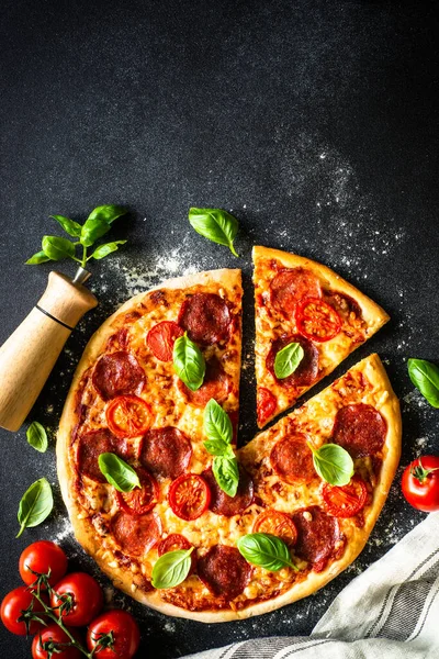 黒テーブルの上にサラミチーズ トマト バジルのピザ コピースペース付きのトップビュー — ストック写真