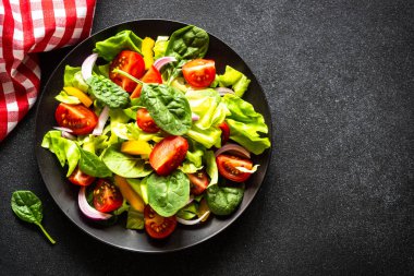 Taze sebzeli yeşil salata ve siyah arka planda yeşil yapraklar. Kopyalama alanı olan üst görünüm.