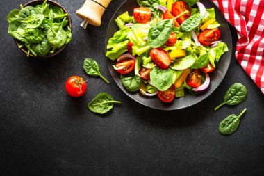 Taze sebzeli yeşil salata ve siyah arka planda yeşil yapraklar. Kopyalama alanı olan üst görünüm.