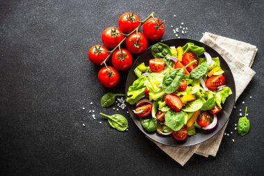 Taze sebzeli yeşil salata ve siyah arka planda yeşil yapraklar. Kopyalama alanı olan üst görünüm.