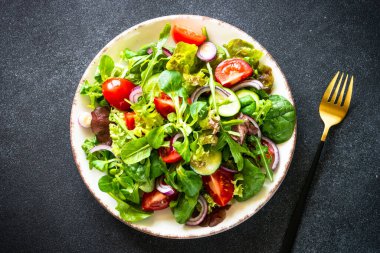 Yeşil salata. Siyah masada beyaz tabakta taze salata yaprakları ve sebzeler. Kopyalama alanı olan en üst görüntü.