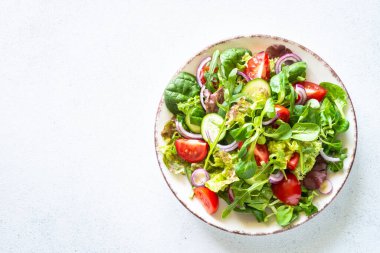 Beyaz tabakta salata. Taze yeşil yapraklar ve sebze salatası. Sağlıklı vejetaryen yemekleri, diyet yemekleri. Üst görünüm, alanı kopyala.