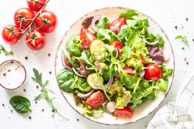 Yeşil salata, sebze yemeği. Taze salata yaprakları ve beyaz tabakta sebzeler. Sağlıklı vejetaryen yemekleri, diyet yemekleri. En üst görüntü.