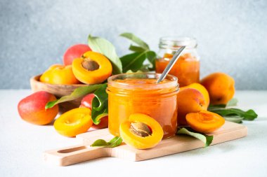 Cam kavanozda kayısı reçeli ve beyaz mutfak masasında taze kayısılar..