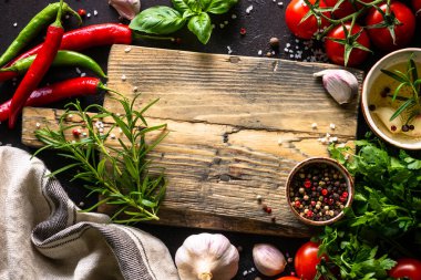 Food background. Oak cutting board, spices and vegetables at dark kitchen table. Top view with space for design.