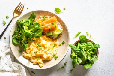 Çırpılmış yumurta, krem peynirli sandviç, somon balığı ve yeşil salata yaprakları beyaz taş masada. Kopyalama alanı olan üst görünüm.