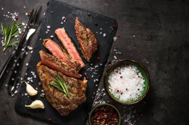 Siyah arka planda biftek. Izgara biftek striploin orta pişmiş, servis tahtasında. Kopyalama alanı olan üst görünüm.