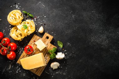 Siyah arka planda makarna malzemeleri. Çiğ makarna, parmesan peyniri, taze domates ve fesleğen. Kopyalama alanı olan üst görünüm.