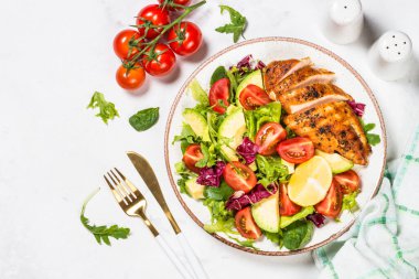 Kızarmış tavuk filetosu, taze yapraklar, avokado ve sebzeli sağlıklı salata. Beyaz mermer masadaki üst görünüm.
