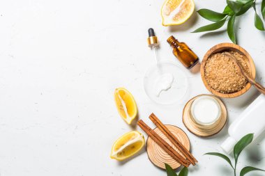 Ev yapımı kozmetik laboratuarı. Kozmetik şişeleri, krem, serum, deniz tuzu, limon ve beyaz masada gerekli yağlar. Kopyalama alanı olan düz resim.