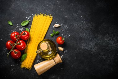 Siyah masada İtalyan yemek geçmişi. Makarna, zeytinyağı, baharat, fesleğen ve taze domates. Kopyalama alanı olan üst görünüm.