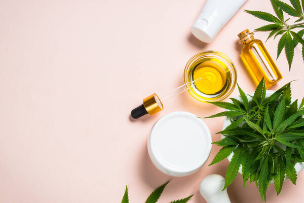 Cannabis oil, cream, cosmetic and fresh green leaves at pink background. Natural cosmetic. Flat lay with copy space.