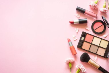 Makeup professional cosmetics on pink background with flowers. Flat lay with copy space.