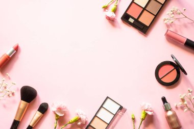 Makeup professional cosmetics on pink background with flowers. Flat lay with copy space.
