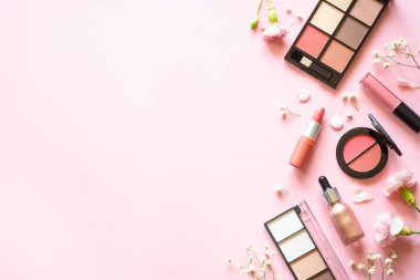Makeup professional cosmetics on pink background with flowers. Flat lay with copy space.