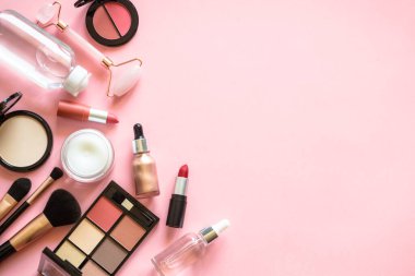 Makeup cosmetic products on pink background. Cream, lipstick, shadow and brushes. Flat lay image with copy space.